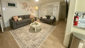Un salon avec deux canapés, une table basse et un tapis à motifs. On y trouve également un ventilateur de plafond et une lampe fixée au mur.