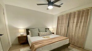 Une chambre à coucher avec un lit, des tables de chevet, un ventilateur de plafond et une fenêtre avec des rideaux.