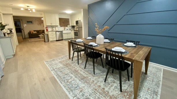 Une cuisine moderne avec des meubles blancs, une table à manger en bois et un mur d’accent bleu.