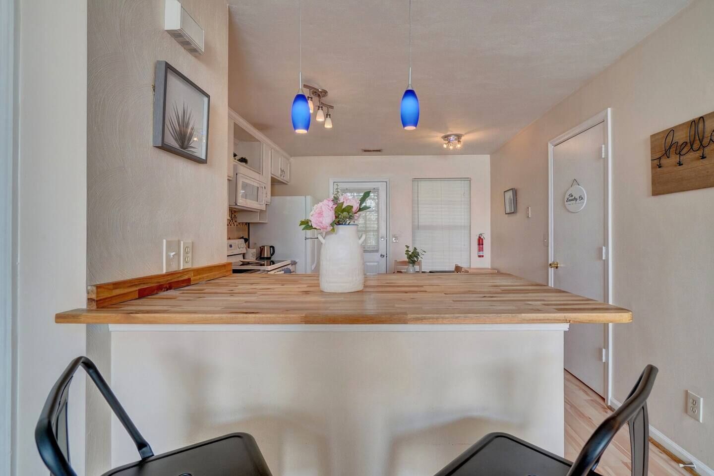Eine Küche mit einer Holztheke, zwei Pendelleuchten und einer weißen Vase mit Blumen.