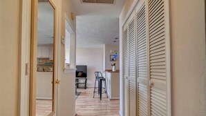 Un corridoio con pavimento in legno, una televisione sullo sfondo e una zona cucina visibile attraverso una porta aperta.