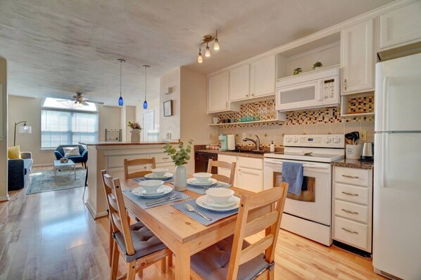 A modern kitchen with white cabinets, a wooden dining table, and a built-in oven.