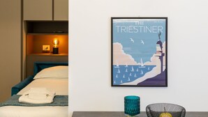 Ein Hotelzimmer mit einem Bett, einem gerahmten Poster an der Wand, einer Nachttischlampe und einem kleinen Tisch mit einem Glasbehälter.