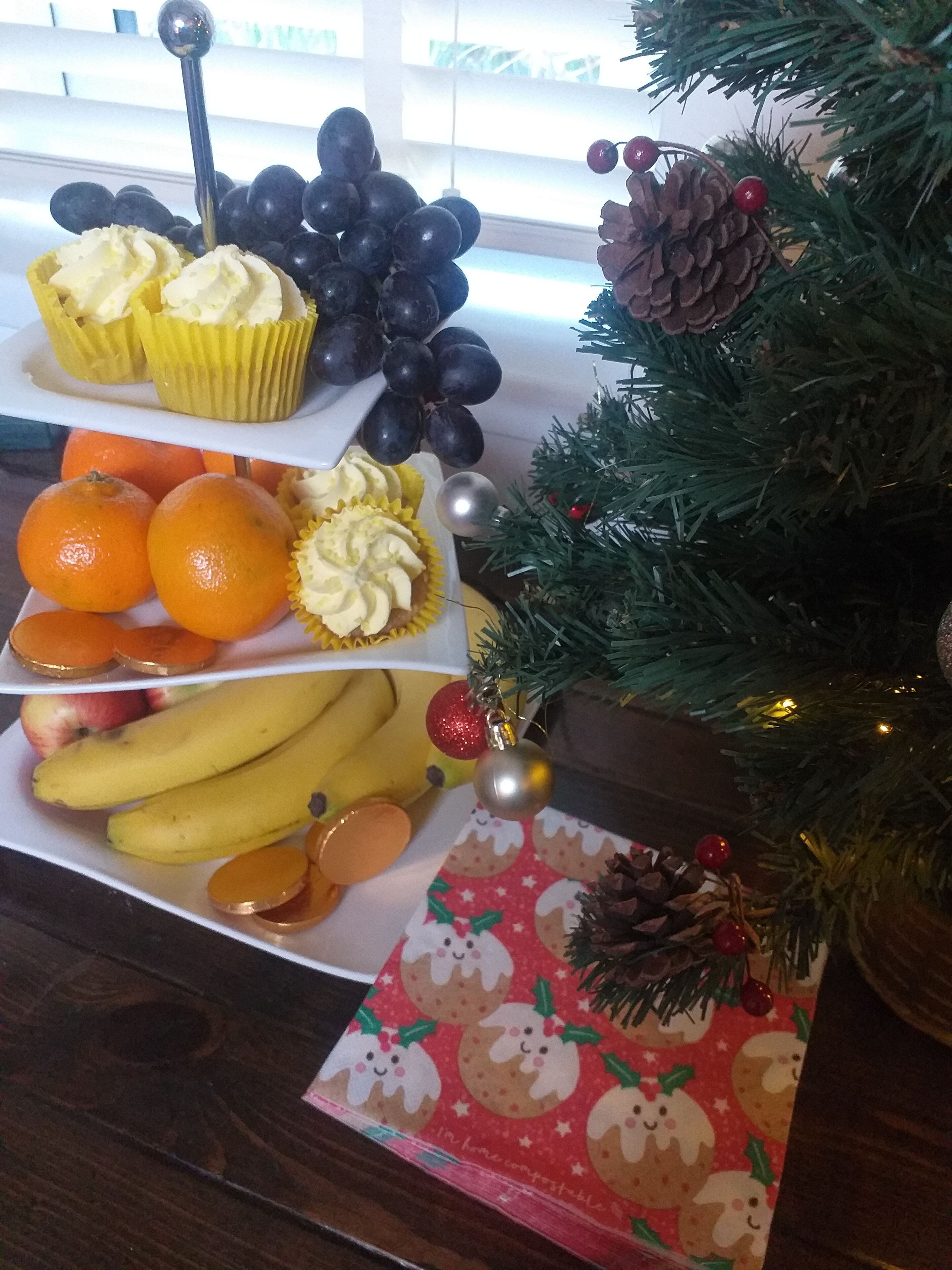 Una bandeja de frutas con uvas, cupcakes, naranjas y plátanos.