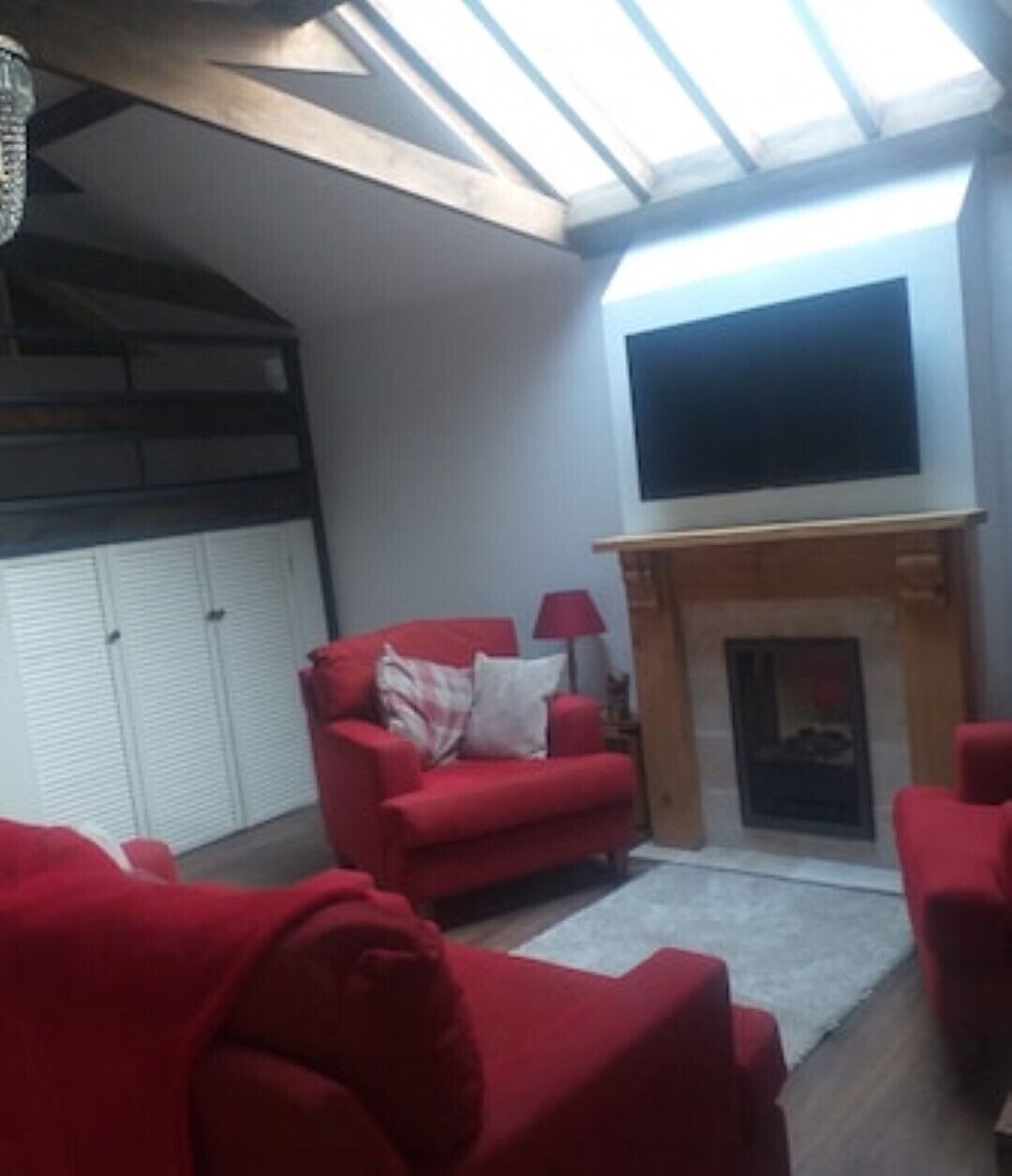 Un salon avec un canapé rouge, une cheminée et un téléviseur fixé au mur.