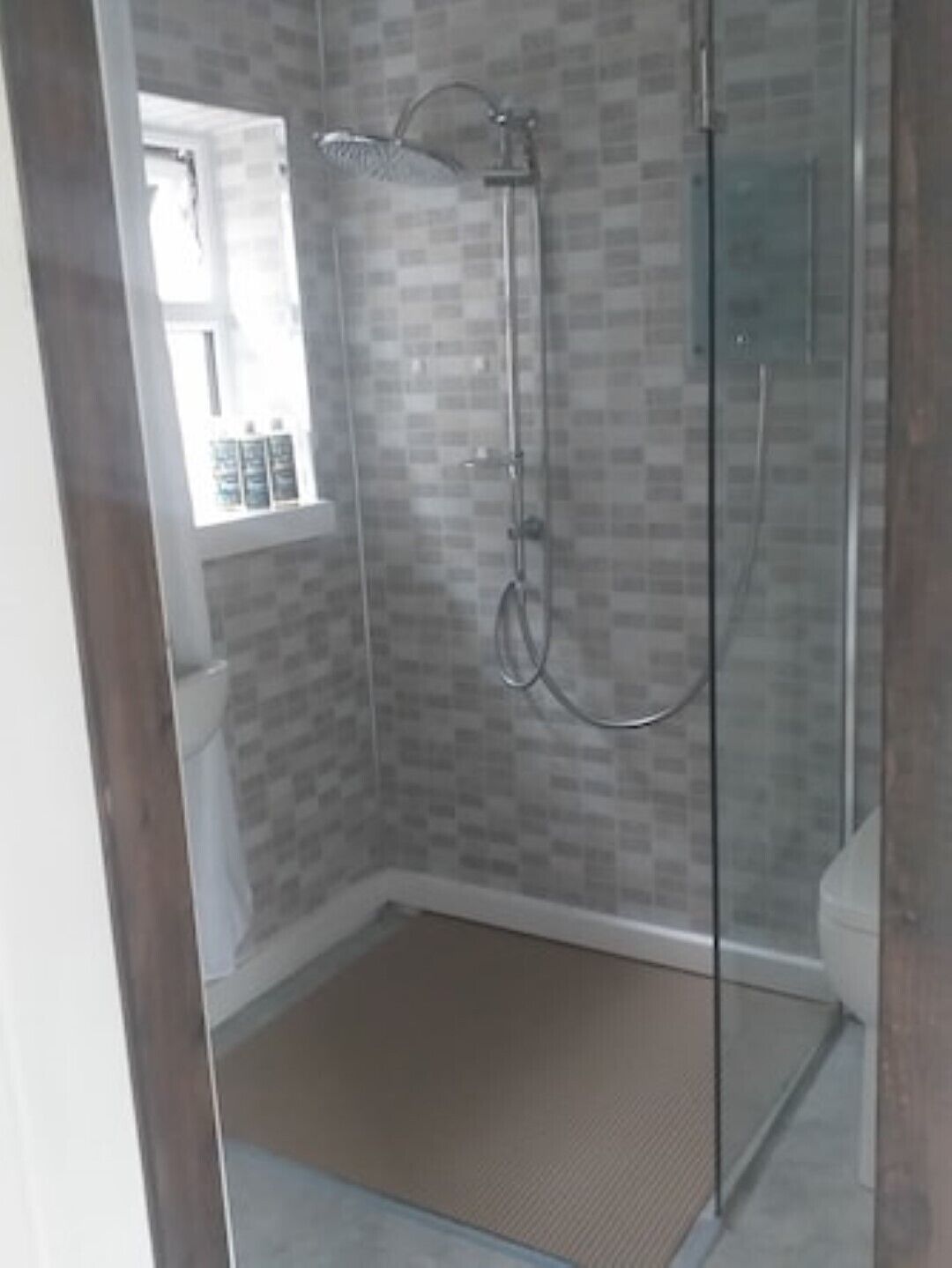 Ein Duschbereich mit Glasabtrennung, einer gefliesten Wand und einem Fenster über der Toilette.