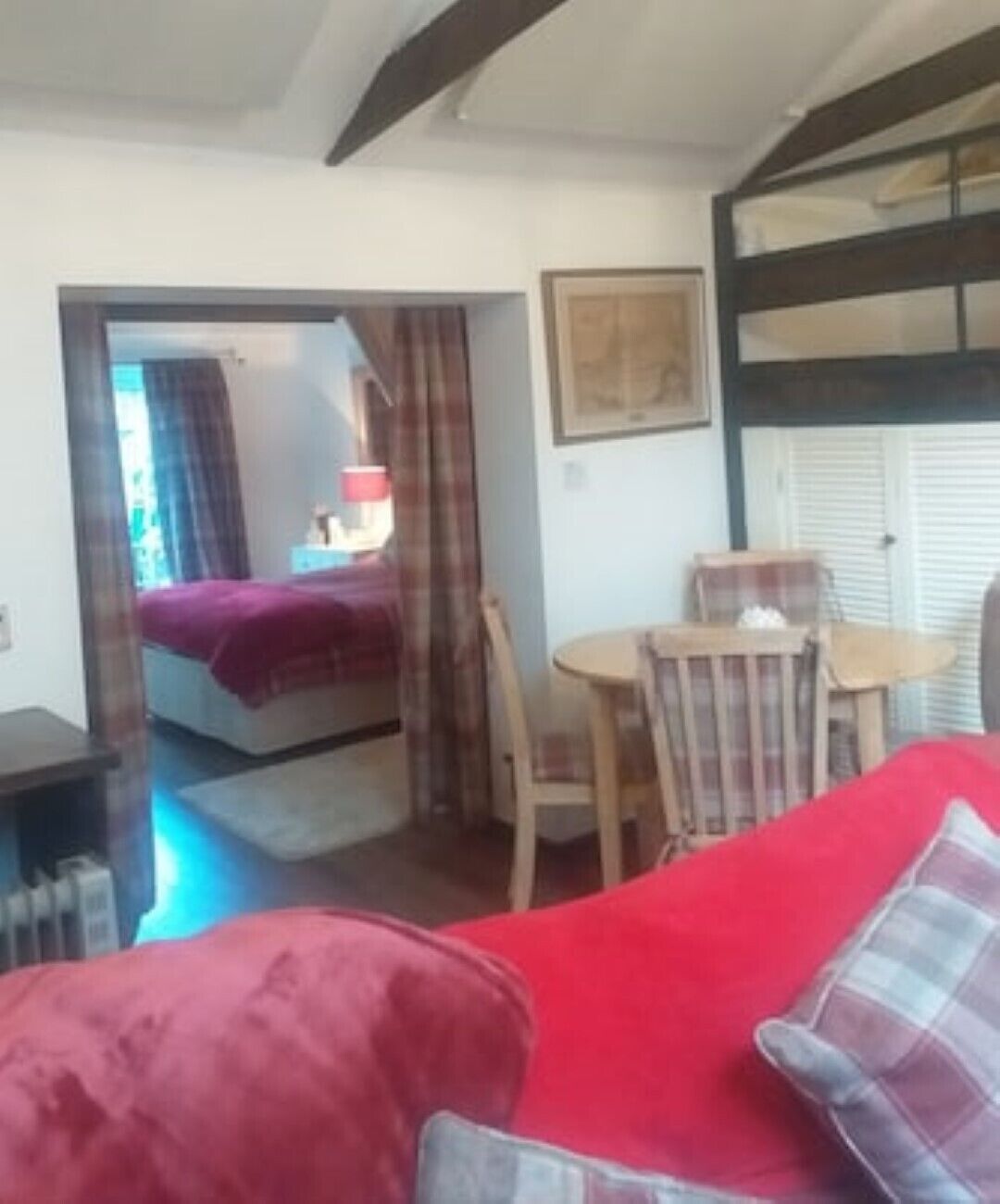 A room with a red sofa, a wooden dining table with chairs, a bed with a purple blanket, and a framed picture on the wall.