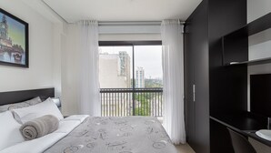 A modern hotel room with a large bed, a desk, and a balcony with a city view. - SB Setin Brooklyn Studios (São Paulo)