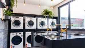 A modern laundry room with multiple washing machines, a sink, and potted plants. - SB Setin Brooklyn Studios (São Paulo)