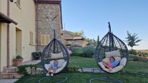 Dos sillas colgantes al aire libre en un jardín, con un edificio de piedra al fondo.