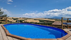 Una terraza de madera con piscina, con vistas a un viñedo y colinas lejanas.