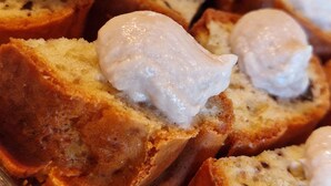 Rebanadas de pan cubiertas con una capa blanca, posiblemente queso crema o mantequilla, dispuestas en una bandeja.