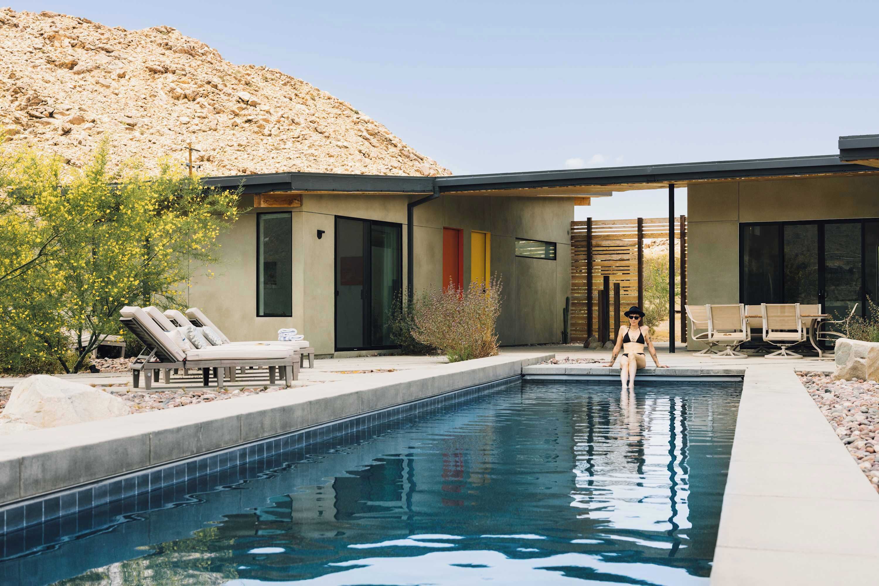 A modern pool area with a clear view of the pool, lounge chairs, and a desert landscape in the background.