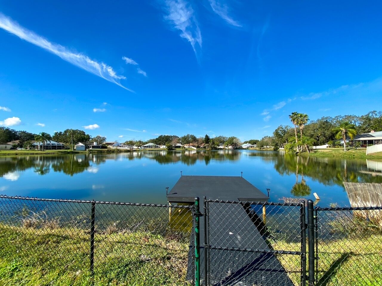 A calm lake with a dock and a chain-link fence in the foreground.
