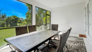 A dining area with a table and chairs, large windows, and a view of greenery outside. - Trendy Naples Retreat: Modern Vacation Home (Naples)