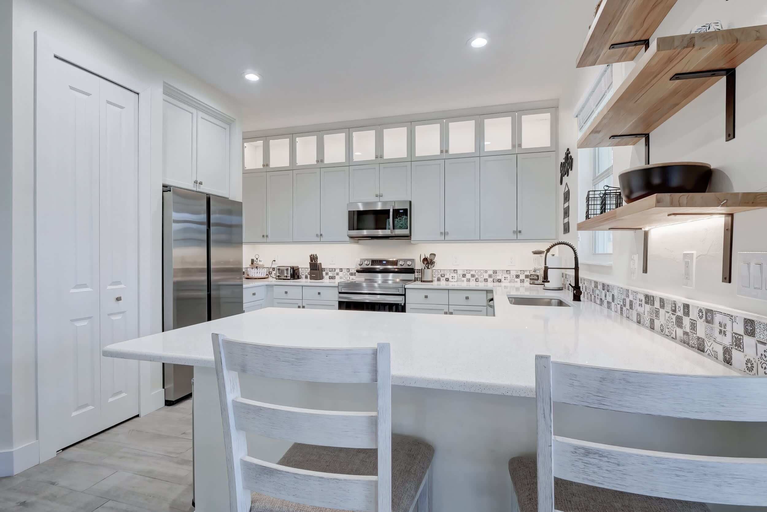 A modern kitchen with white cabinetry, a central island, stainless steel appliances, and a backsplash with a geometric pattern.