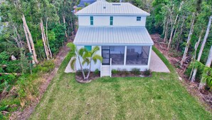 A two-story house with a large glass front, surrounded by a well-maintained lawn and dense tropical vegetation. - Trendy Naples Retreat: Modern Vacation Home (Naples)