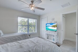 A bedroom with two beds, a ceiling fan, a TV on a white cabinet, and a window with blinds.