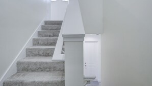 A staircase with carpeted steps leading to a landing, white walls, and a door at the bottom. - Trendy Naples Retreat: Modern Vacation Home (Naples)