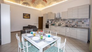 A modern kitchen with white cabinets, a tiled backsplash, and a dining area with a white table set for four. - Casato Diciannove, a few steps from Piazza del Campo (Siena)