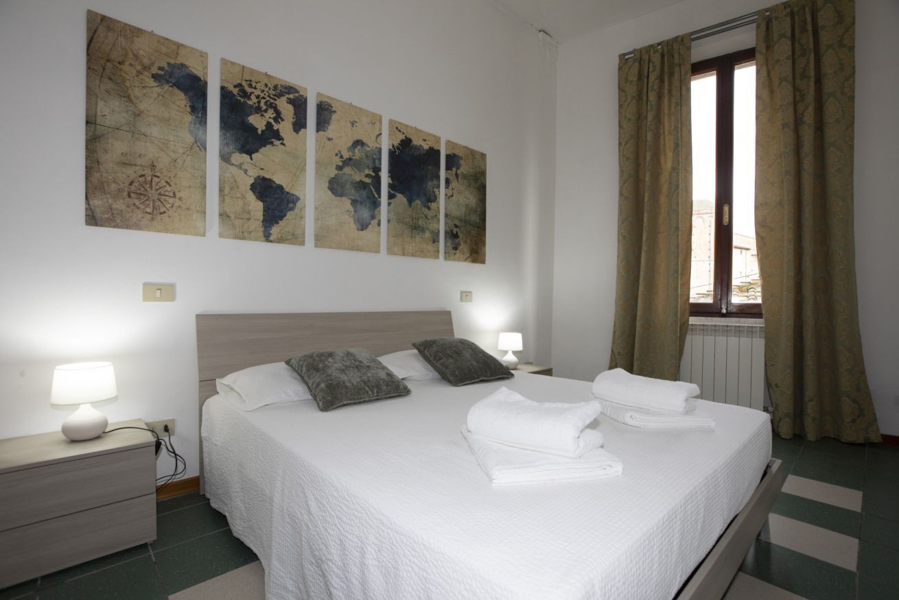 Uma cama bem arrumada com lençóis e almofadas brancos, uma cabeceira de madeira e uma obra de arte com um mapa mundi acima.