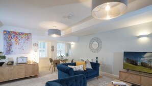 A spacious living room with a blue sofa, a dining area, and a large painting on the wall.