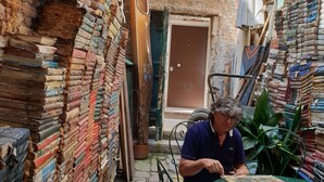 A narrow alley with stacks of books on both sides, a green table, and a person sitting at the table. - "BIGHOUSE" VENICE CENTER NEW AND LUXURY FLAT (Venezia)