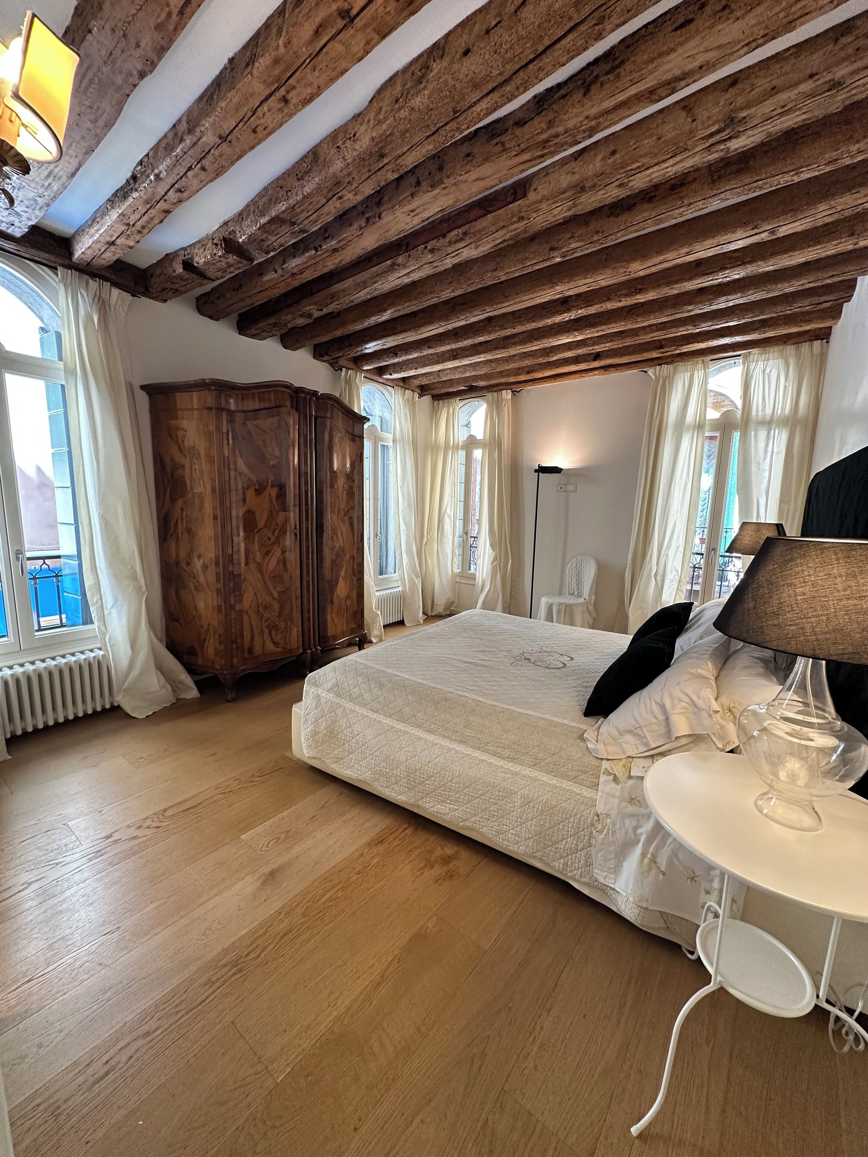 A bedroom with a wooden ceiling, a large bed, a wardrobe, and a bedside table with a lamp.