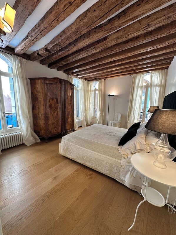 A bedroom with a wooden ceiling, a large bed, a wardrobe, and a bedside table with a lamp.