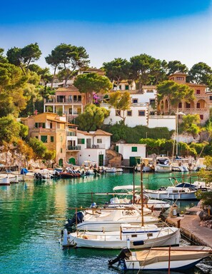 A coastal village with traditional architecture, a marina with boats, and lush greenery. - Ikos Porto Petro – All inclusive (Santanyi)