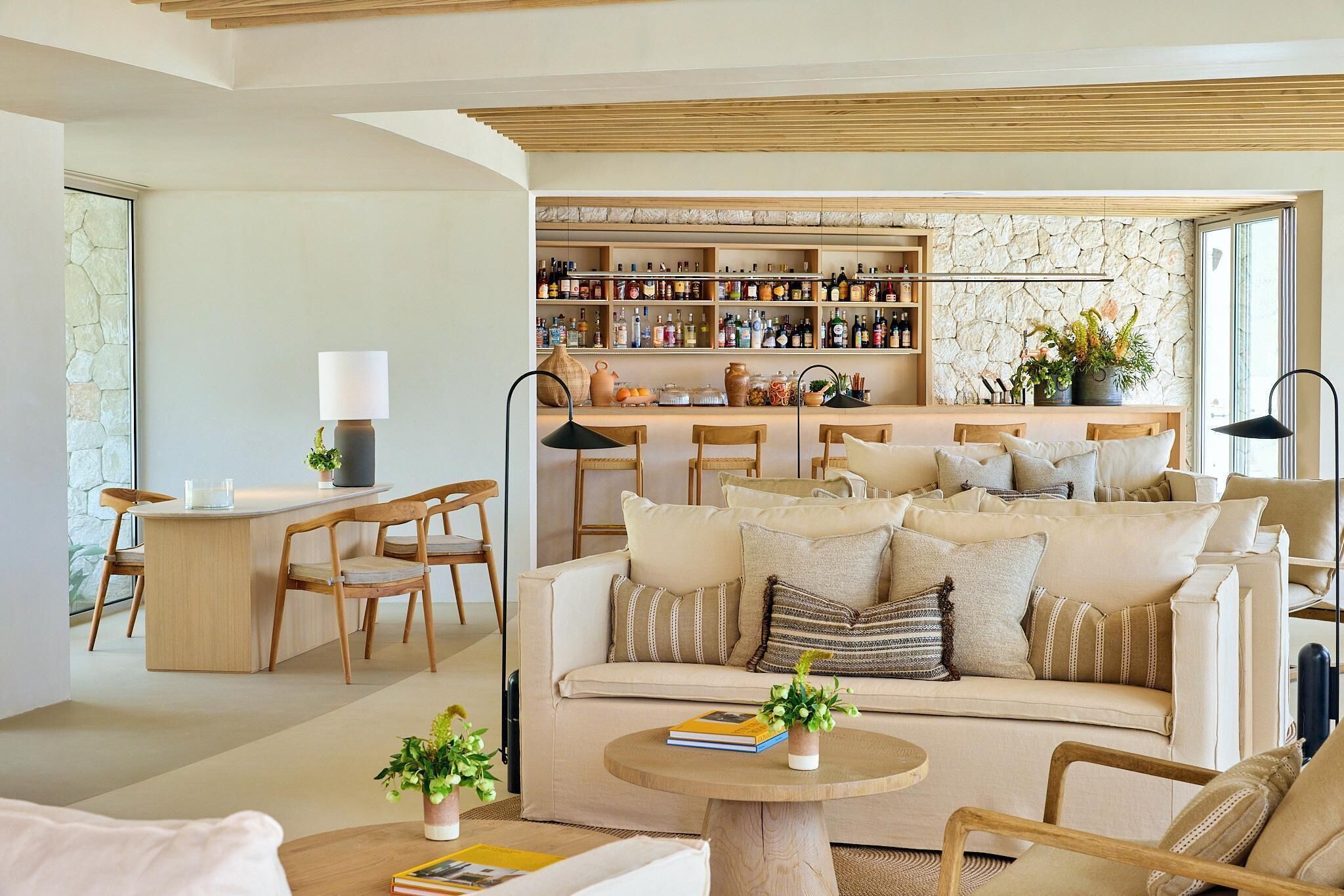 A modern living room with a sofa, chairs, a coffee table, and a bar area with shelves of bottles.