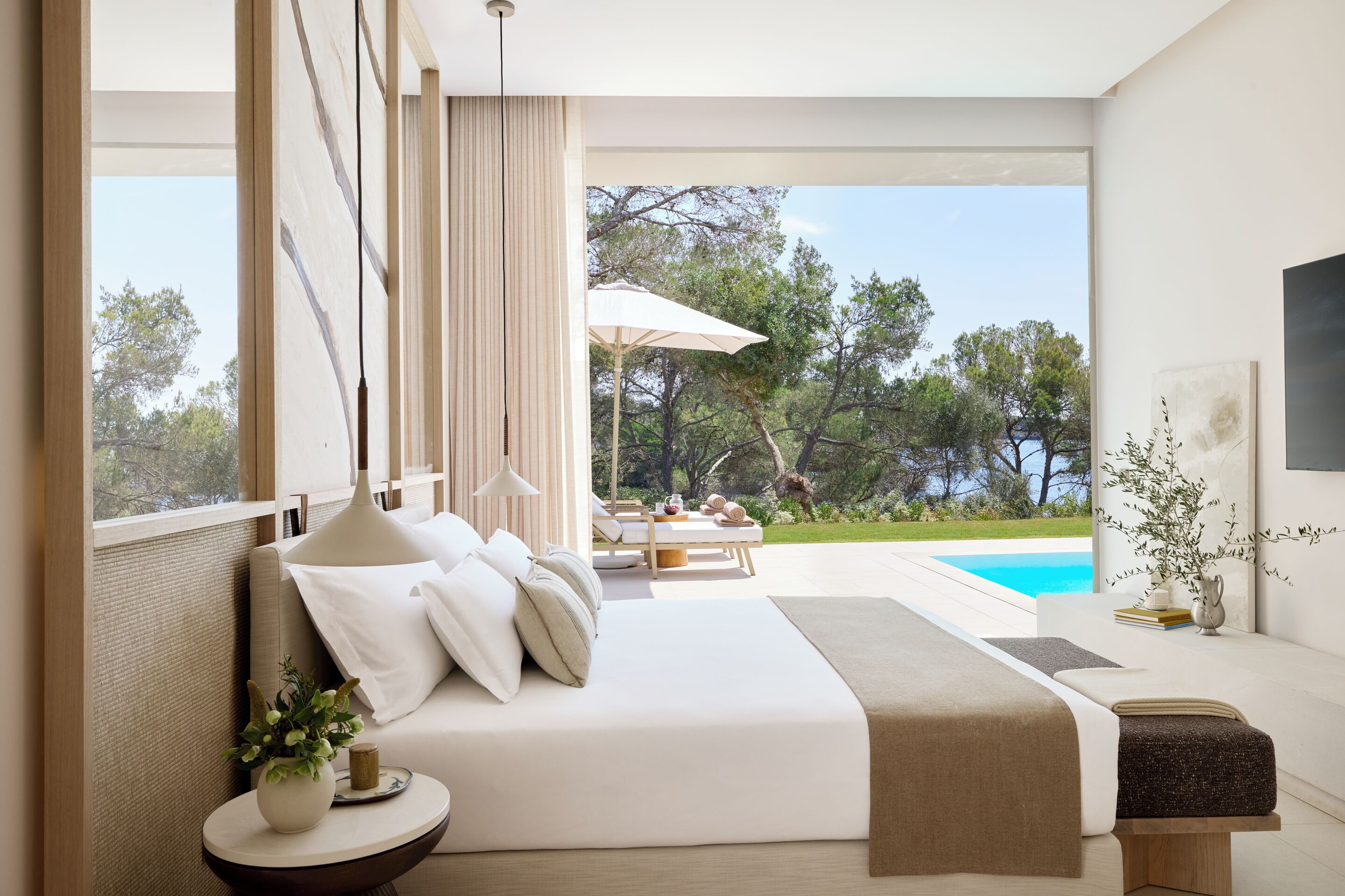 Un dormitorio moderno con una cama grande, una mesita de noche con una planta y vistas a una piscina y zona de estar al aire libre.