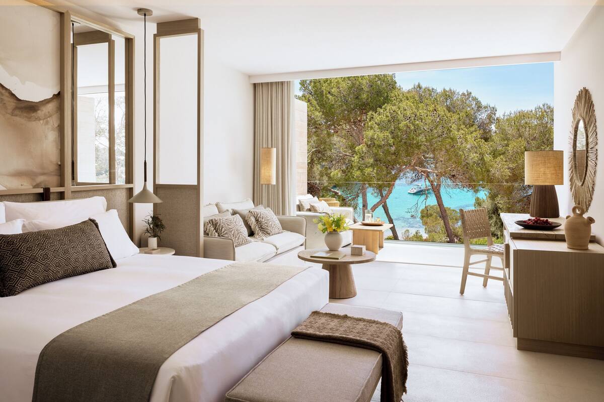 A modern hotel room with a large bed, a sofa, a desk, and a view of a body of water.