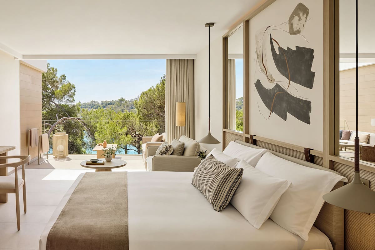 A hotel room with a bed, a desk, a chair, a small table, a sofa, and a view of the outdoors.