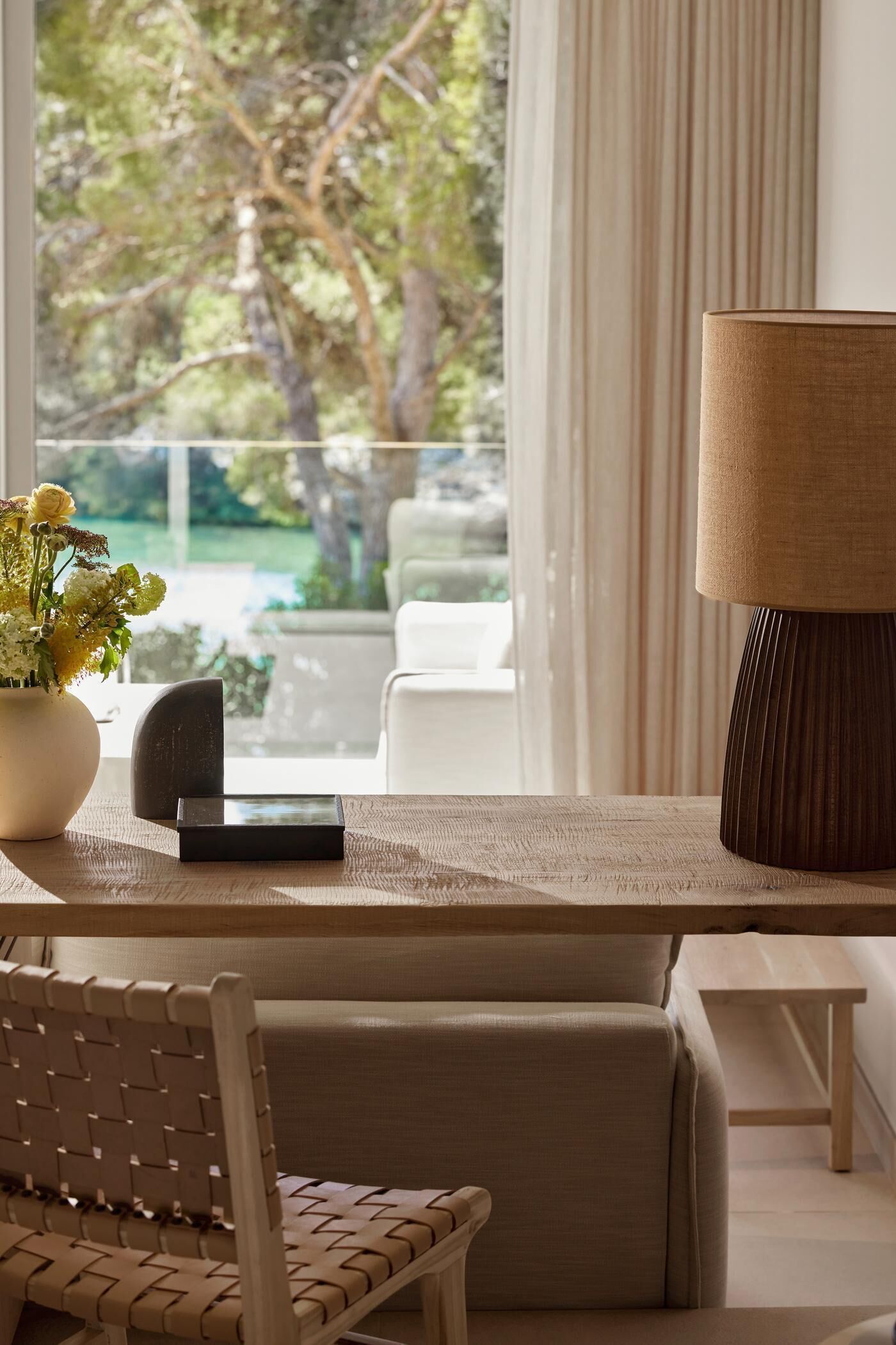 Ein modernes Wohnzimmer mit Blick auf einen Garten, ein Sofa, ein Tisch mit Lampe und eine Blumenvase.