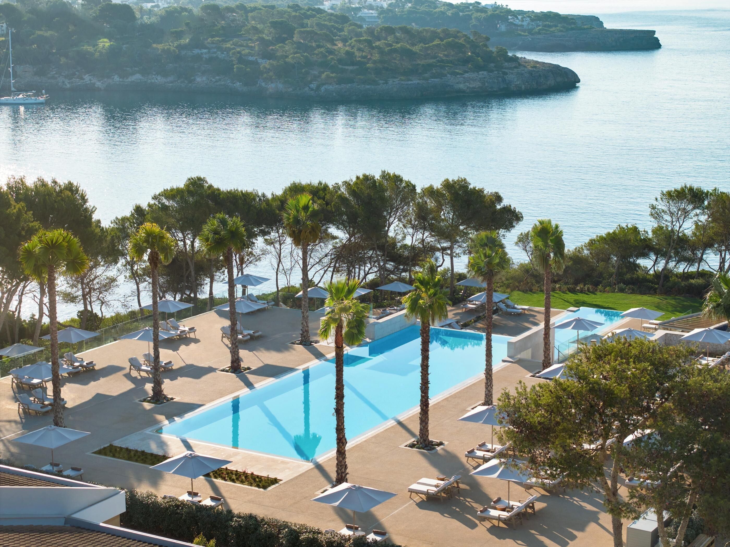 Un resort con una piscina grande, sillas de sol, sombrillas y vista al mar.