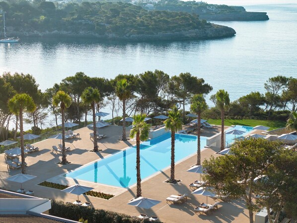 A resort with a large pool, sun loungers, umbrellas, and a view of the sea. - Ikos Porto Petro – All inclusive (Santanyi)