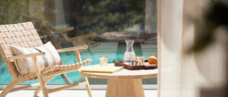 A wooden lounge chair with a cushion, a round wooden table with a tray, and a glass vase.