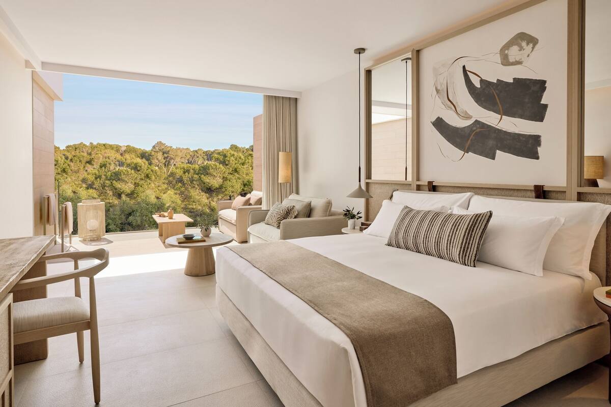 A modern hotel room with a large bed, a desk, and a balcony with a view of the forest.