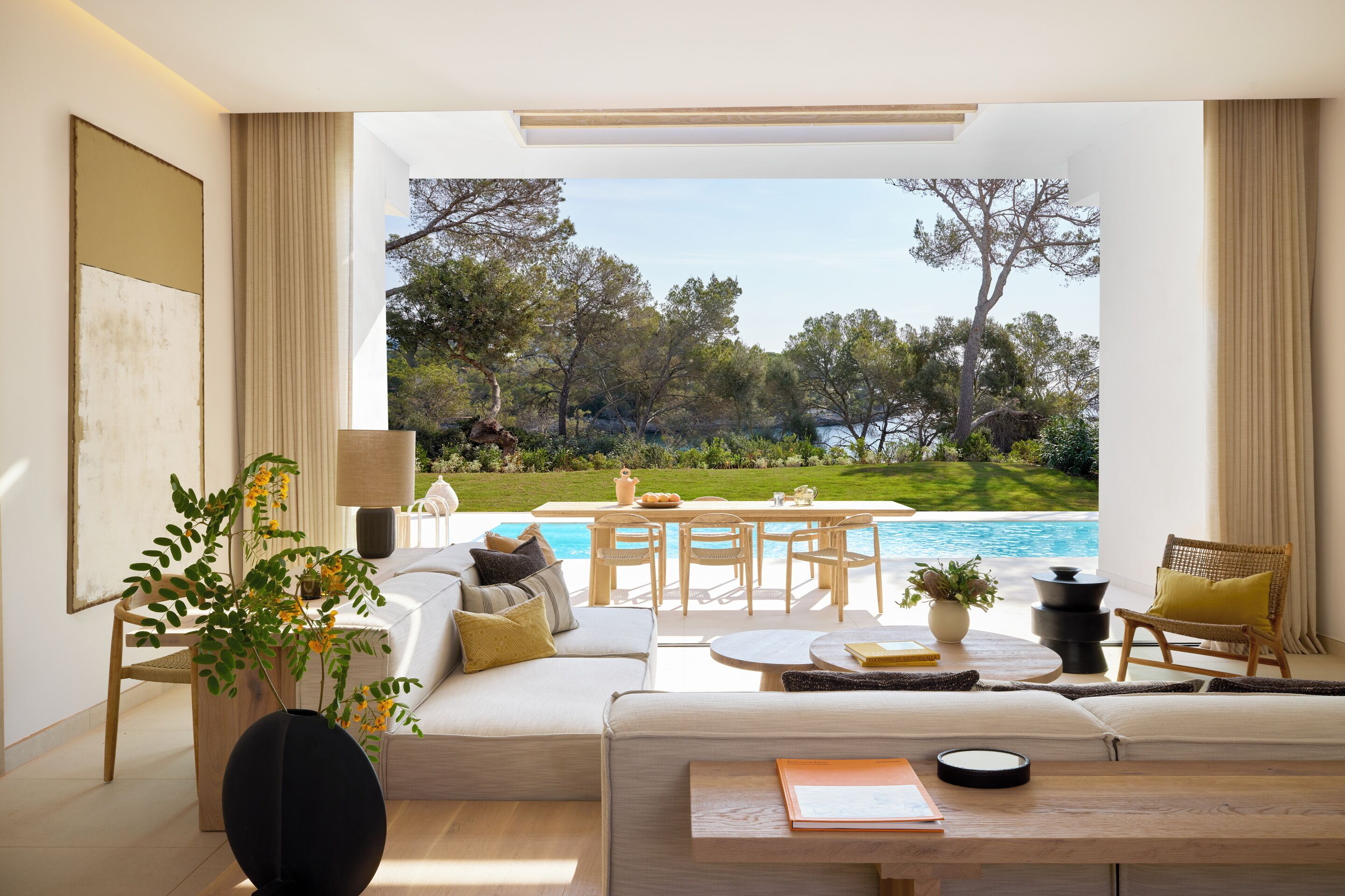 A modern living room with a sofa, coffee table, and a view of a pool and garden.