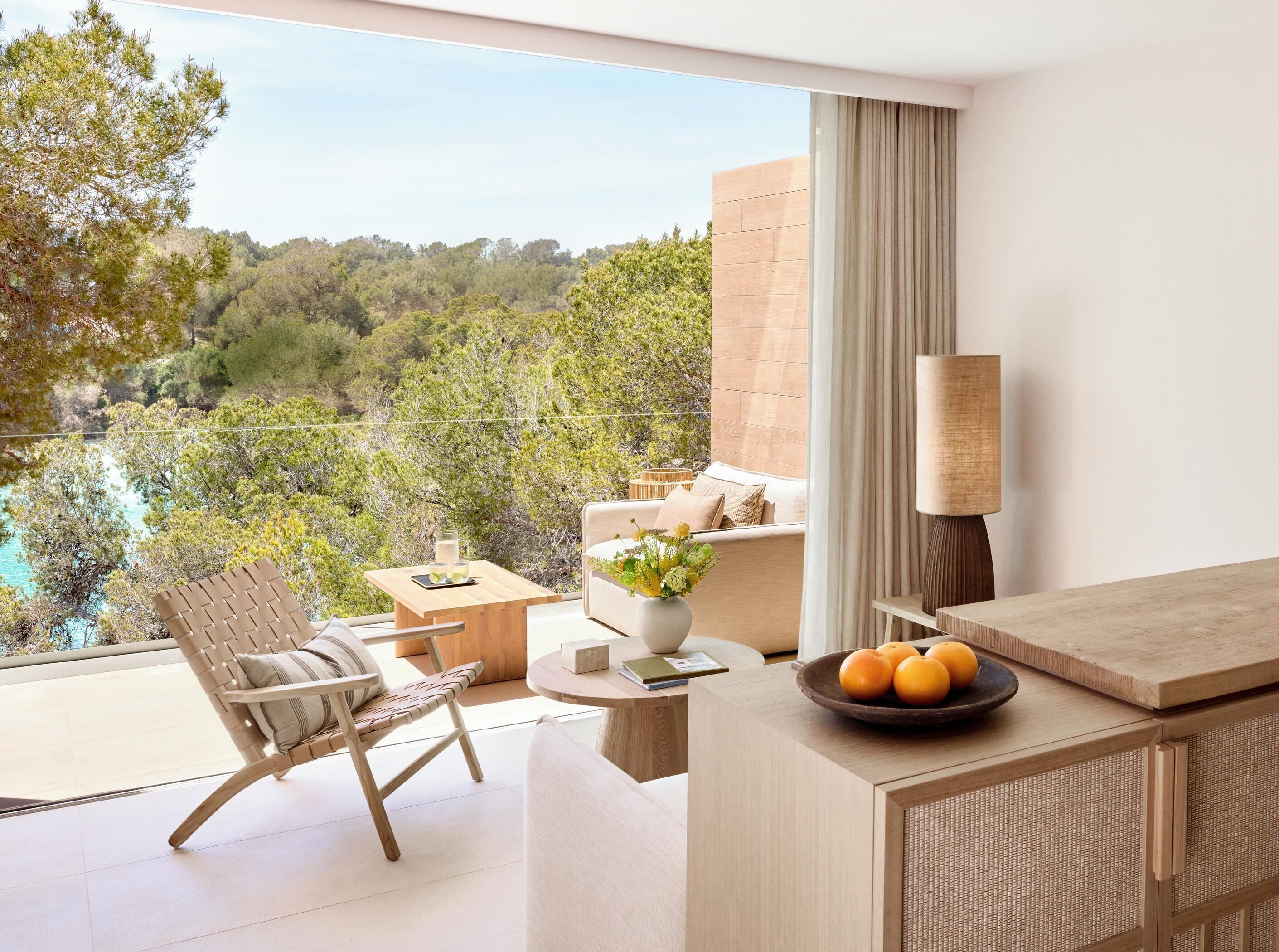 A modern room with a balcony overlooking a forested area and a pool.