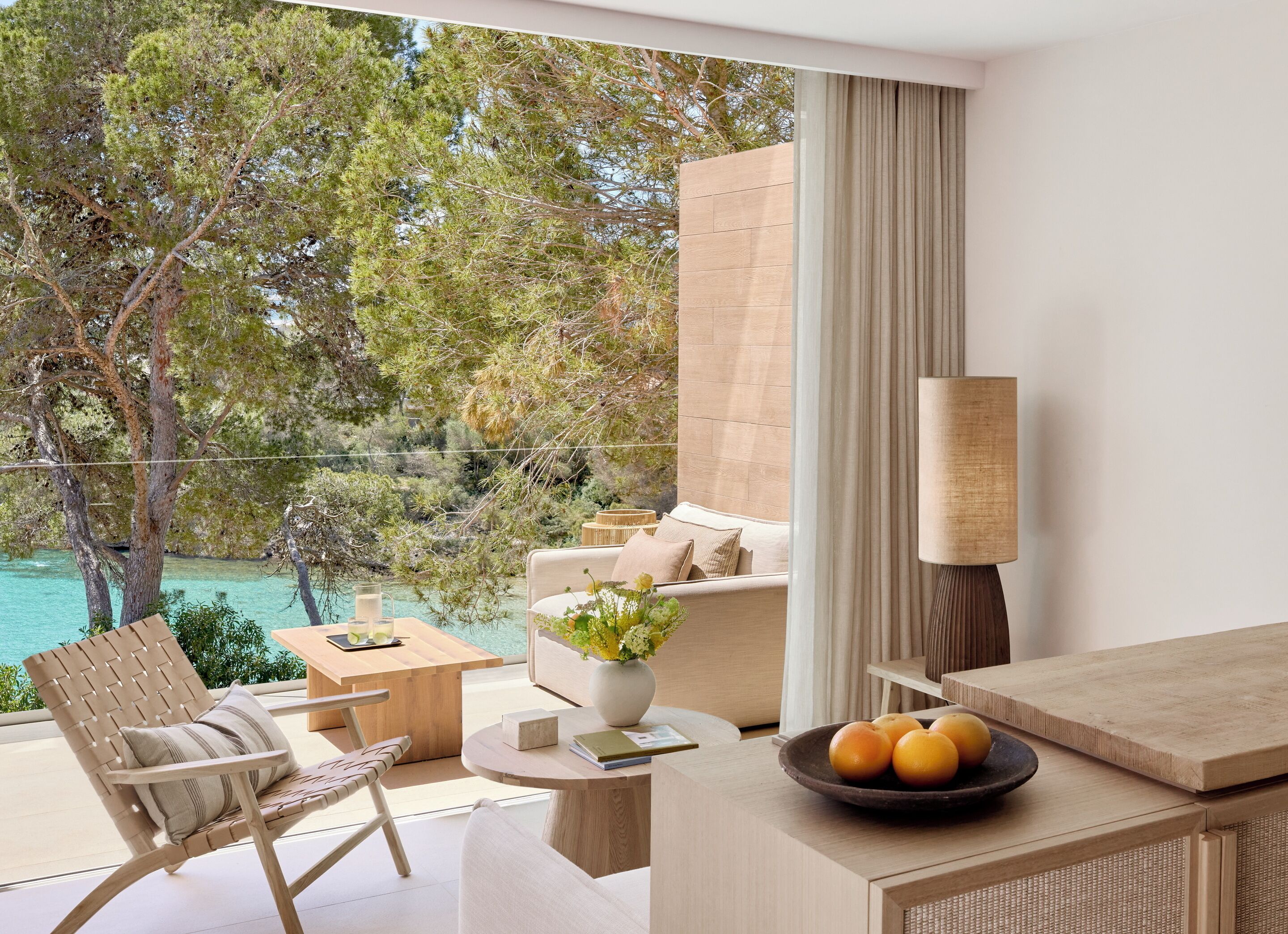 A modern hotel room with a balcony, a sofa, a dining table, and a lamp.