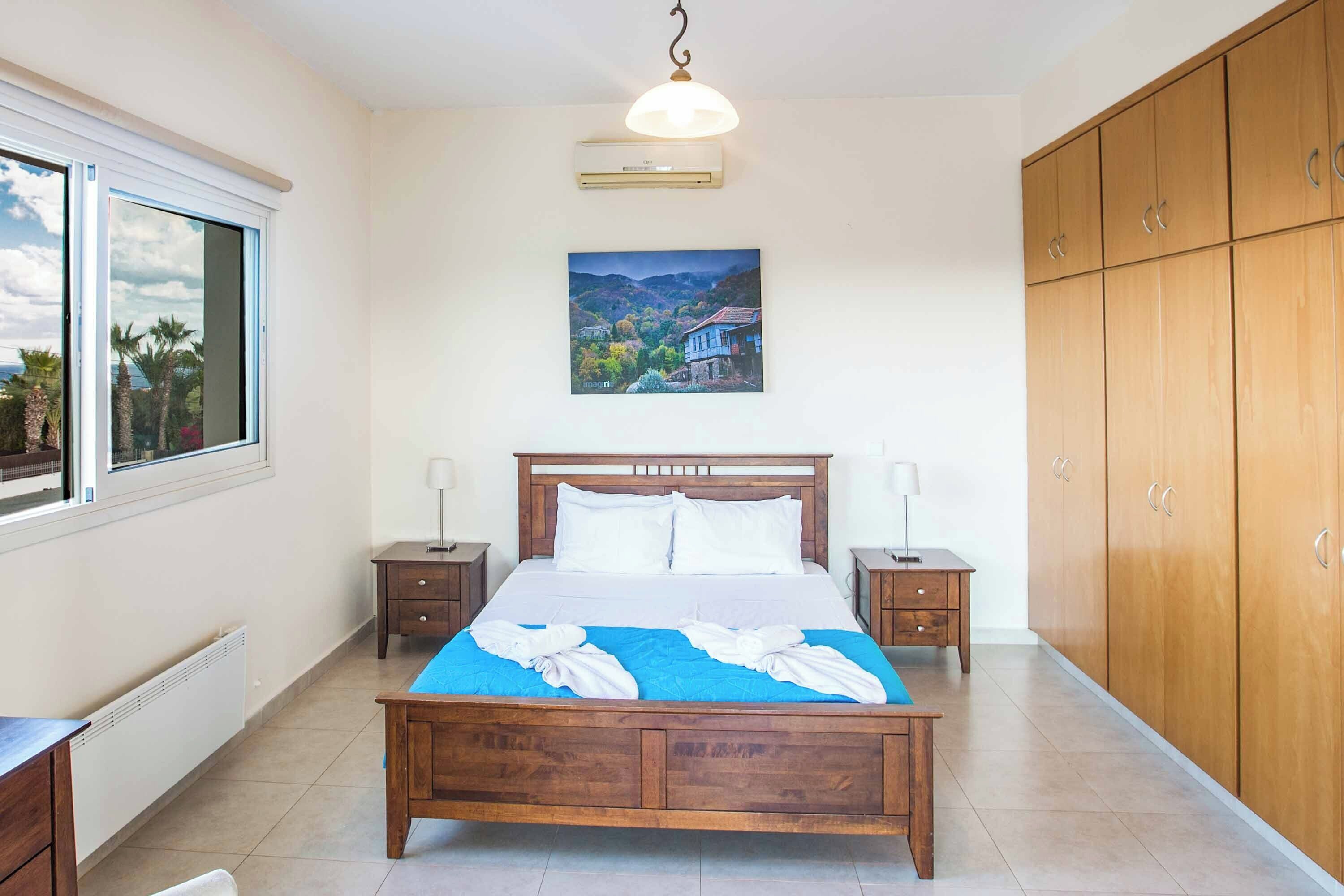 A bedroom with a large bed, wooden wardrobe, and a window with a view of a landscape.