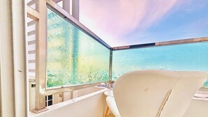 Ein Balkon mit einem weißen Stuhl, einem kleinen Tisch und Blick auf Grün hinter einer satinierten Glasscheibe.