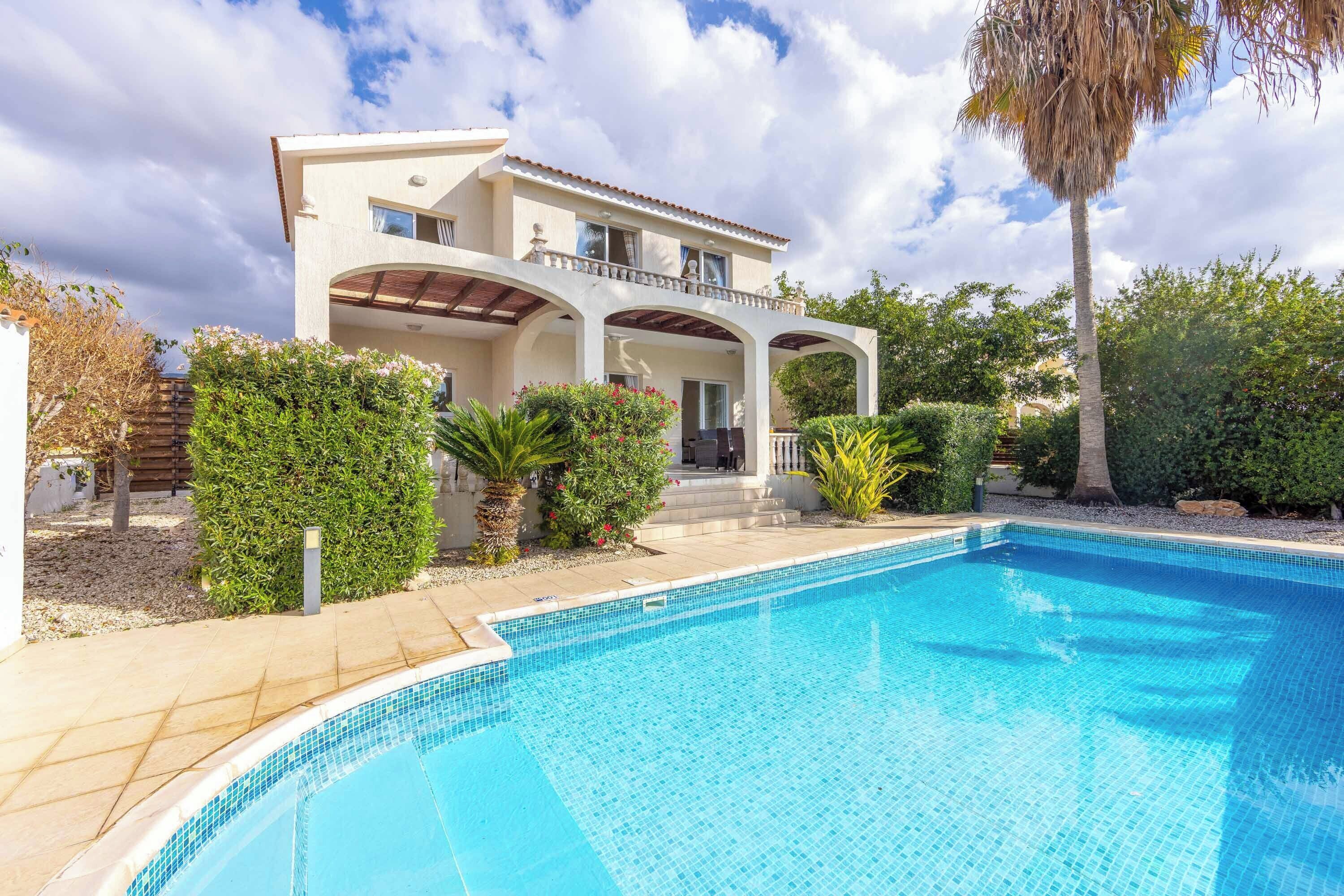 A two-story house with a swimming pool, surrounded by greenery and a clear sky.