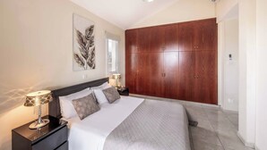 A bedroom with a bed, nightstands, a large wardrobe, and a ceiling light. - Villa Ambrosia - Three Bedroom Villa, Sleeps 6 (Peyia)