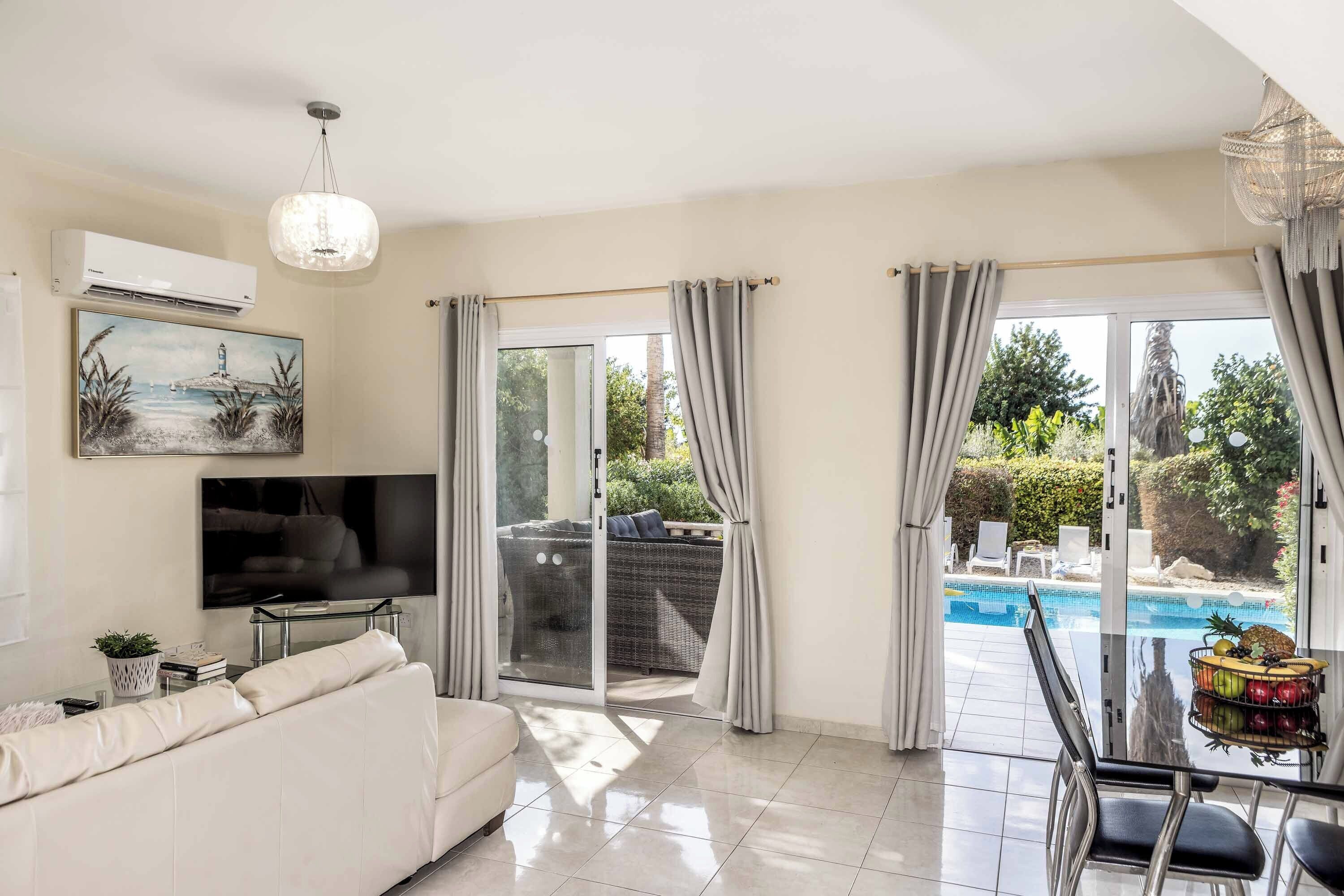 A modern living room with a white sofa, a flat-screen TV, and a glass table with a fruit bowl.