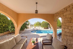 Eine überdachte Terrasse mit Pool, Sitzgelegenheit im Freien und Blick auf den Poolbereich.