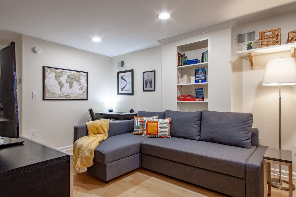 Uma sala de estar moderna com um sofá modular cinza, uma televisão de tela plana, uma mesinha e uma estante com diversos objetos.