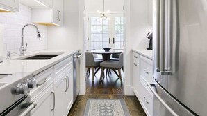 A modern kitchen with white cabinetry, stainless steel appliances, and a dining area with a table and chairs. - Historic, Charming Home in Old Town (Alexandria)
